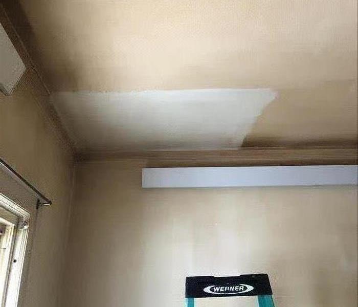A ceiling that is mostly orange/brown with a square white patch. The top of a ladder is below.