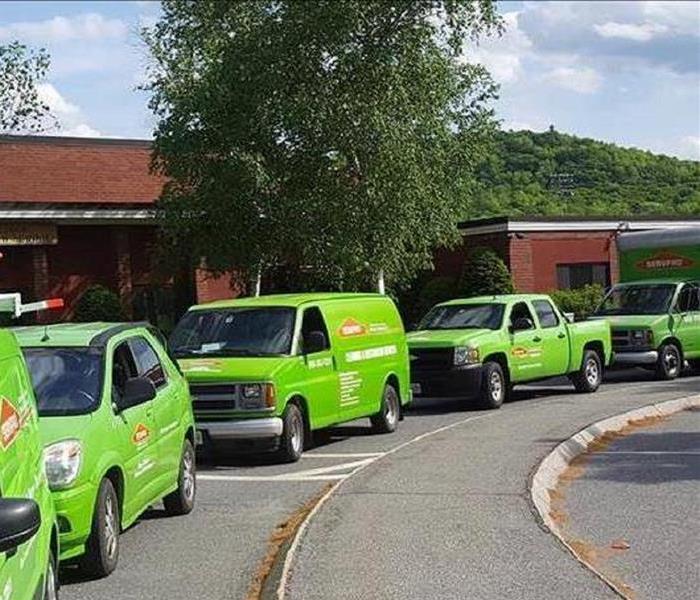 A row of green SERVPRO vehicles lined up in front of a local educational facility to perform cleaning.