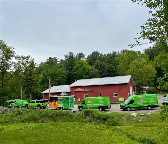 Row of green trucks arranged in front of large red building.