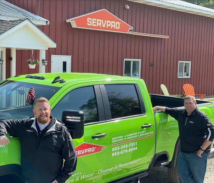 Two employees standing in front of green SERVPRO truck in front of large red building.