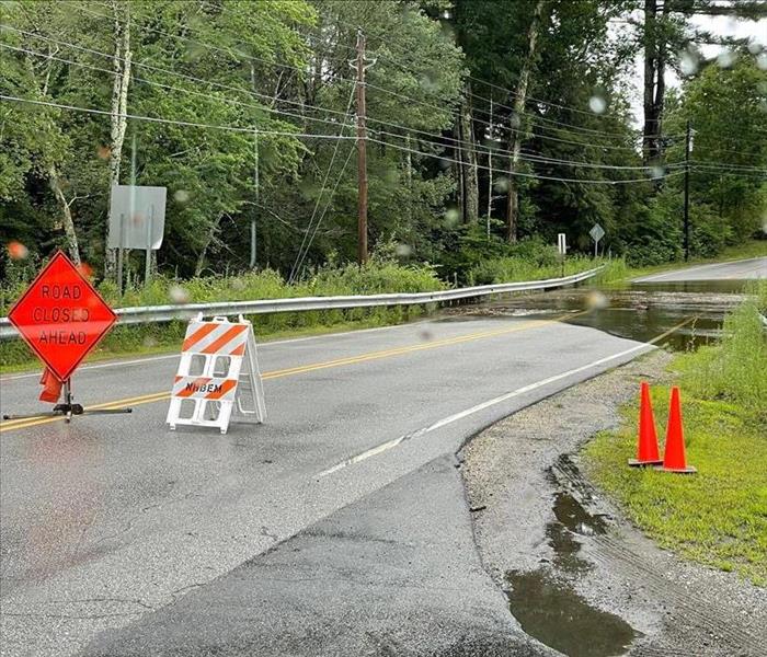 Orange road closure signs on a road which has been flooded due to large amounts of rain.