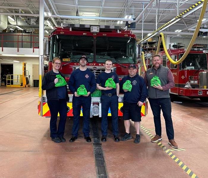 Four firefighters and a SERVPRO representative posing in front of a fire engine.