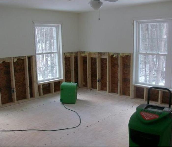 Room which has flooring and base of walls removed with two large dehumidifiers in the room to dry.