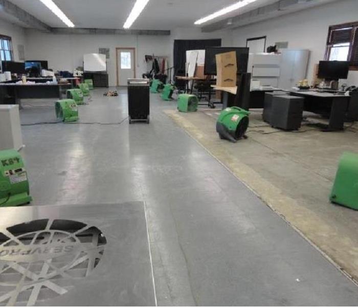 Commercial office space with several large green fans and dehumidifiers installed for drying.