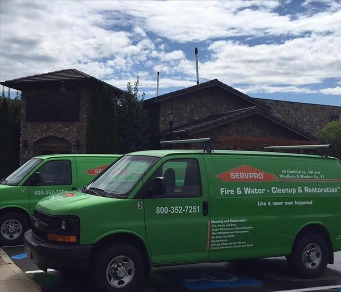 Two green SERVPRO trucks parked in front a brick and stone building.