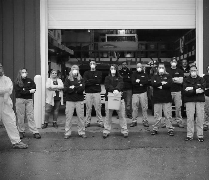 Black & white photo of an entire staff of employees standing in front of open overhead door of warehouse.