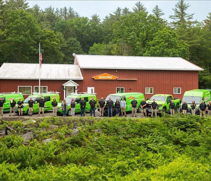 Row of green vans and company staff in front of large red building.