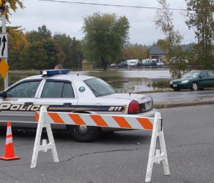 Police cruiser parked in front of a blocked off road due to flooding.